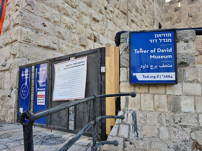 Los letreros para el Museo de la Torre de David, en las afueras de la Ciudad Vieja, junto al hueco del muro de la Puerta de Jaffa y la torre noroeste de la Ciudad Antigua de Jerusalén. Foto: Sasha1506/CC BY-SA 4.0, via Wikimedia Commons.